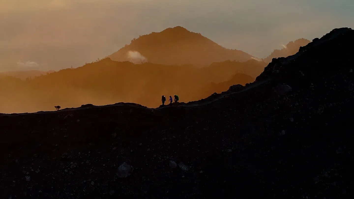 Three hikers silhouetted on the Raung crater rim at sunrise